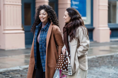 Cheerful multiethnic women walking with gift bags on street