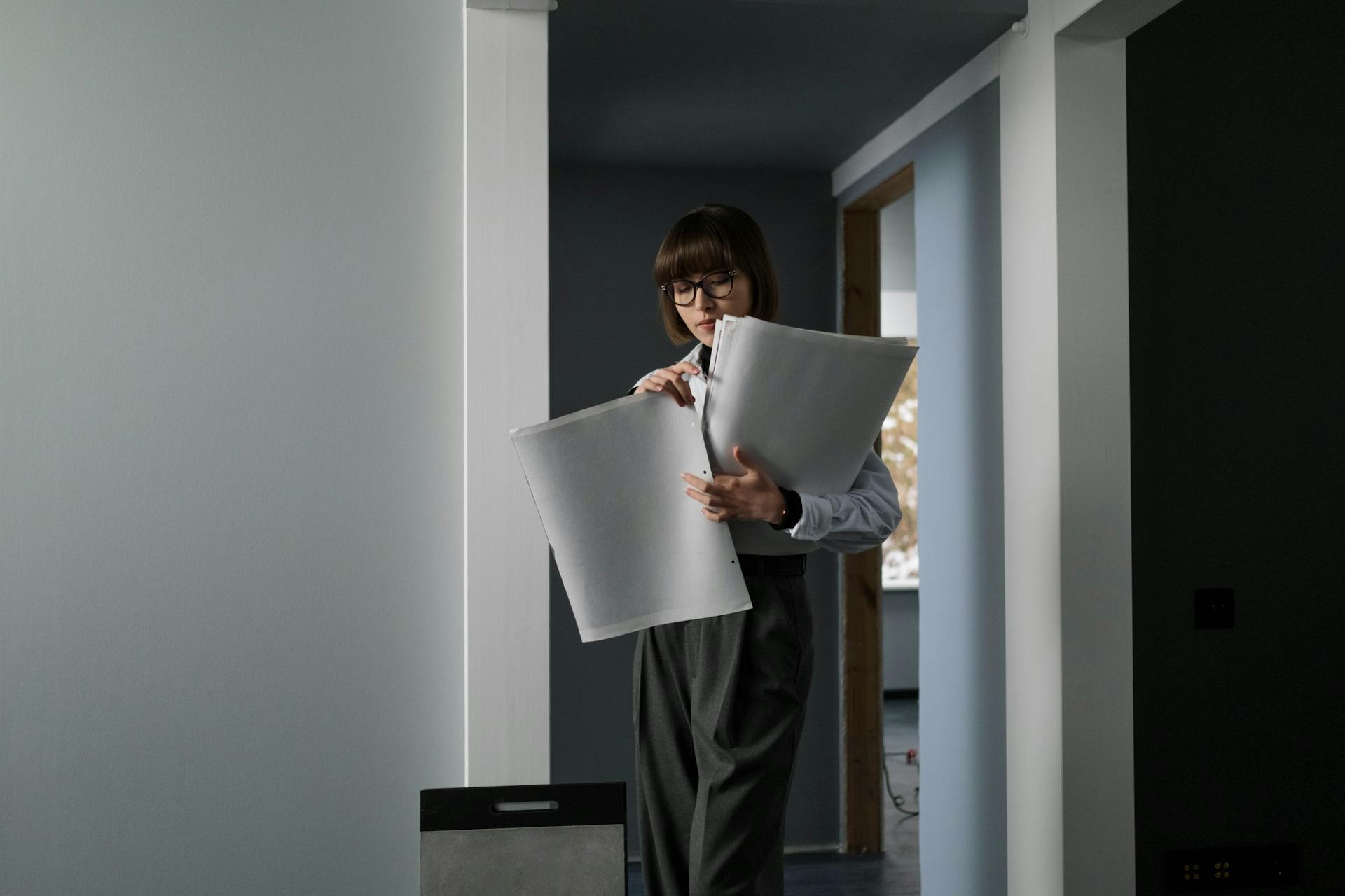 Female architect with eyeglasses examining blueprints in an indoor setting.