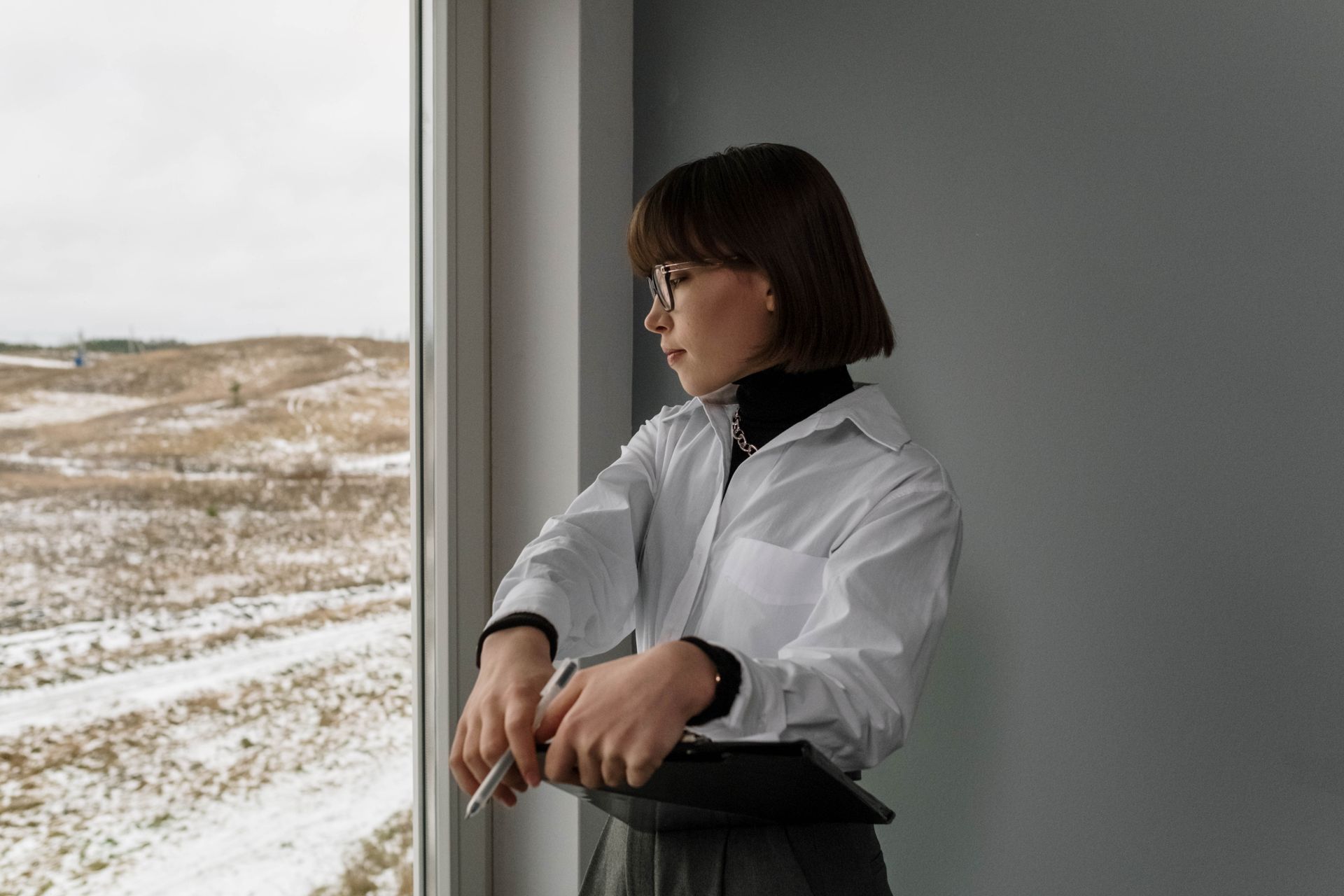 Architect looking outside a window on a snowy winter day, holding a clipboard.