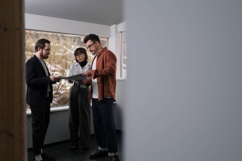 Free Three adults discussing a project inside a well-lit modern office setting. Stock Photo