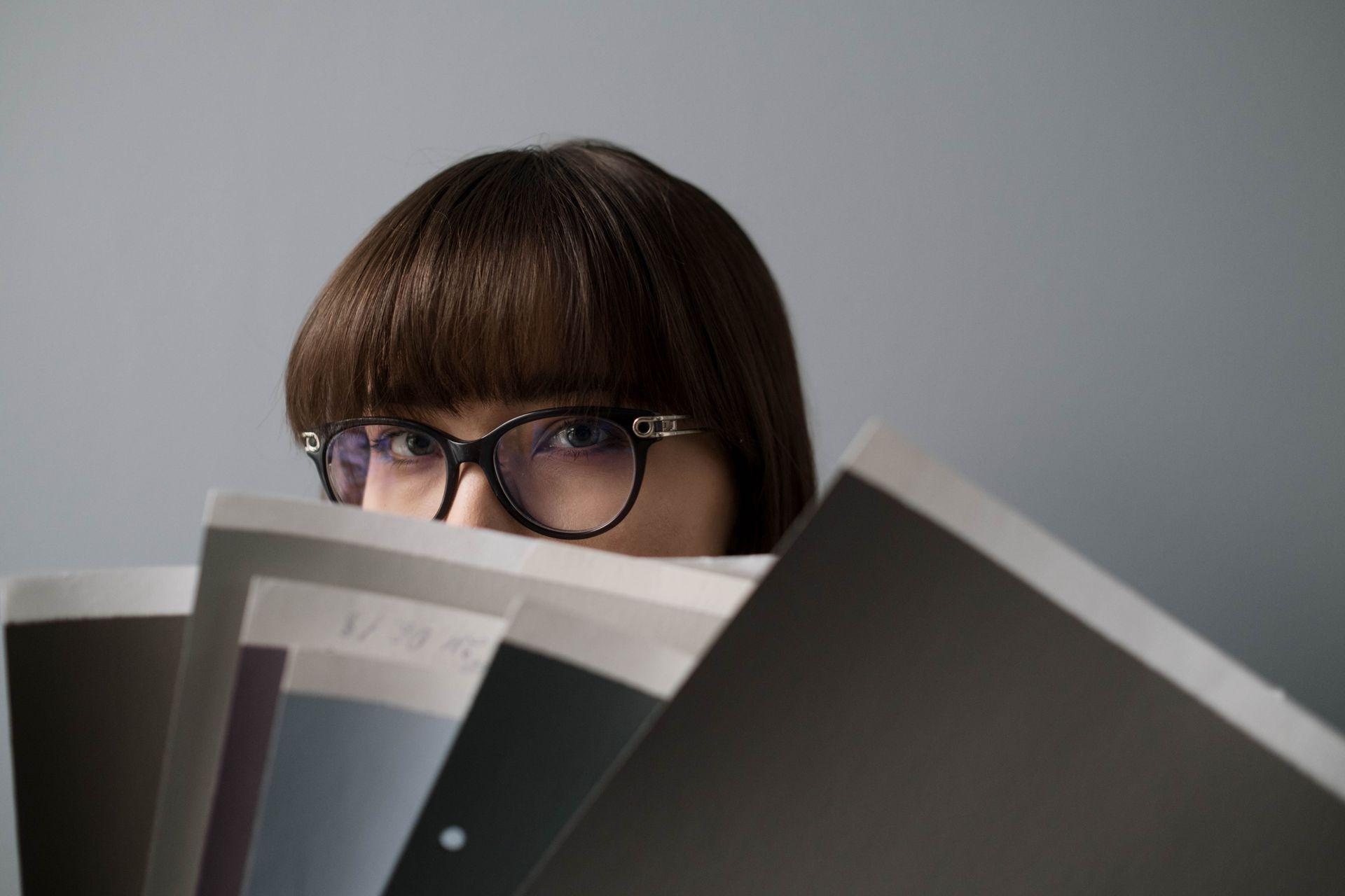 A professional woman wearing eyeglasses intently reviewing multiple documents in a modern office setting.