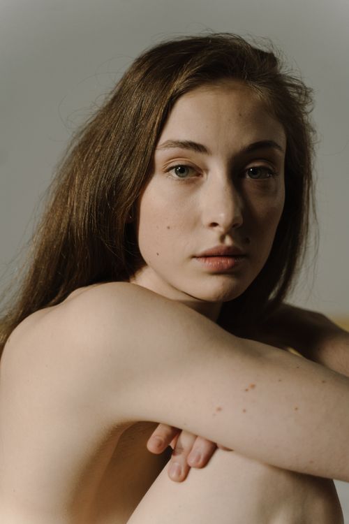 Free Intimate portrait of a woman with long brown hair sitting against a neutral background, evoking a sense of introspection. Stock Photo