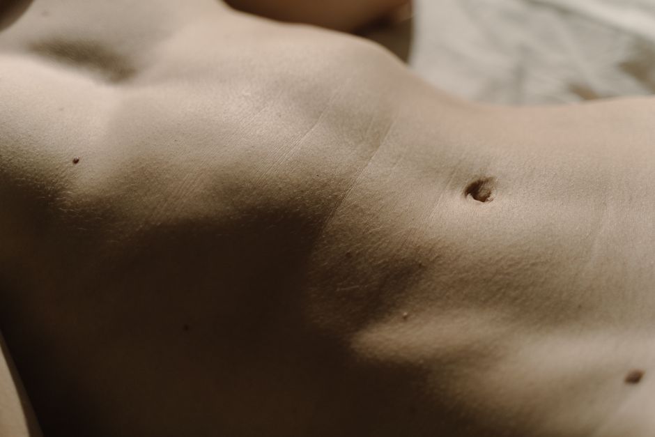 Detailed close-up of human skin featuring belly button, texture, and moles under natural light.
