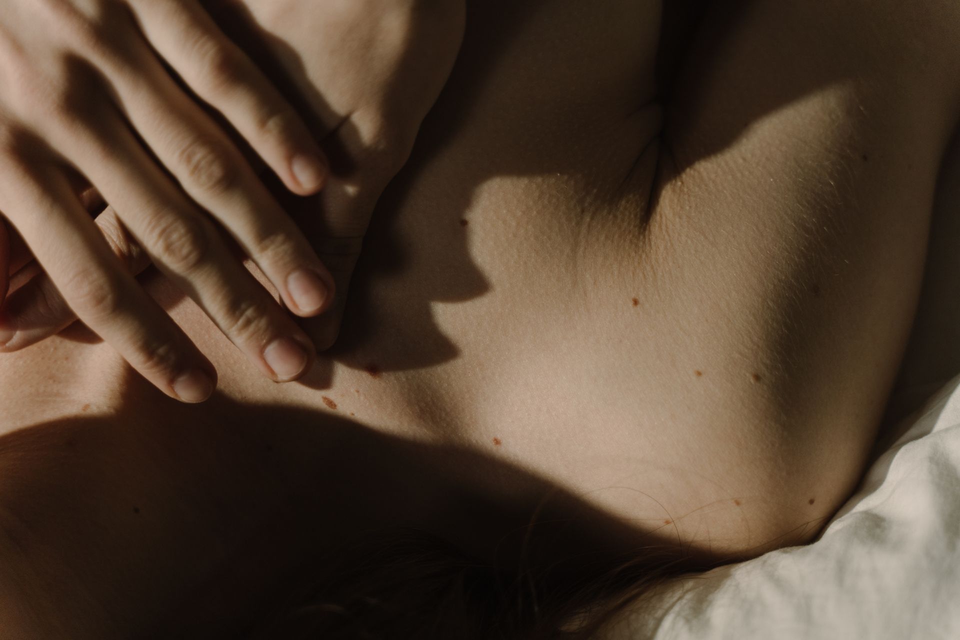 A gentle hand resting on skin with soft natural light creates a peaceful and intimate mood.