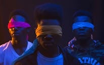 Anonymous cool ethnic male band with Afro hairstyle and covered eyes illuminated by artificial light