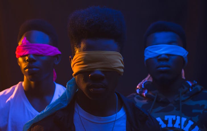 Anonymous cool ethnic male band with Afro hairstyle and covered eyes illuminated by artificial light