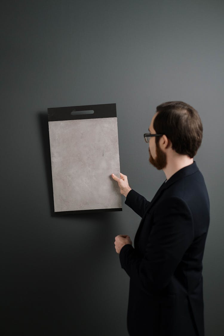 A Man Comparing The Color Of A Sample To A Wall