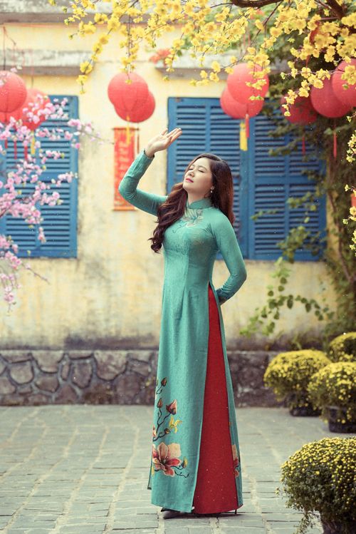 Free Woman in traditional Vietnamese Ao Dai poses gracefully amongst vibrant spring blooms and lanterns. Stock Photo