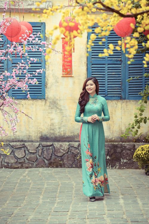 Free A smiling woman in a floral ao dai stands amidst vibrant blossoms and lanterns. Stock Photo