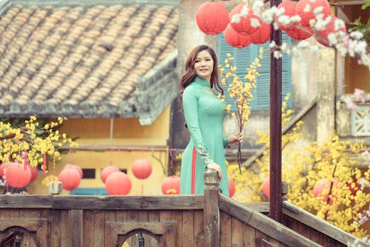 Asian woman in ao dai posing with flowers and lanterns on a wooden bridge.