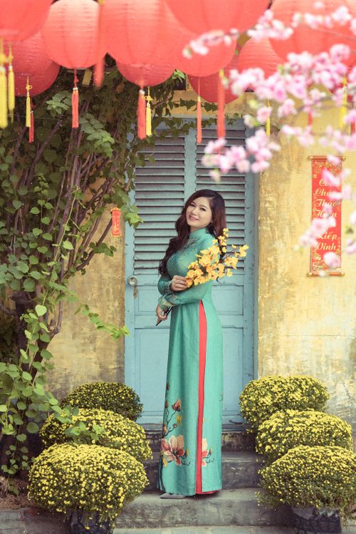 Free Young woman in traditional Vietnamese dress with yellow flowers, standing amidst lush decorations. Stock Photo