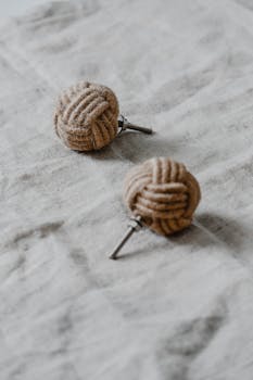 Close-up of textured yarn ball earrings on a soft fabric background, highlighting minimalist design.
