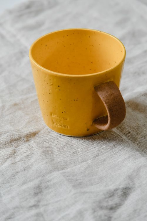 Free A close-up of a yellow ceramic mug with a brown handle on a textured cloth. Stock Photo