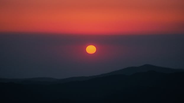 A tranquil sunrise over mountains with a beautiful red and orange sky.