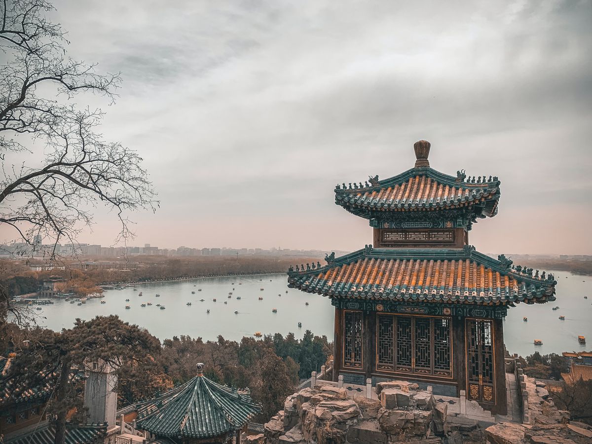 Traditional red-and-gold Chinese pavilion and willows reflected in a calm lakeside city park