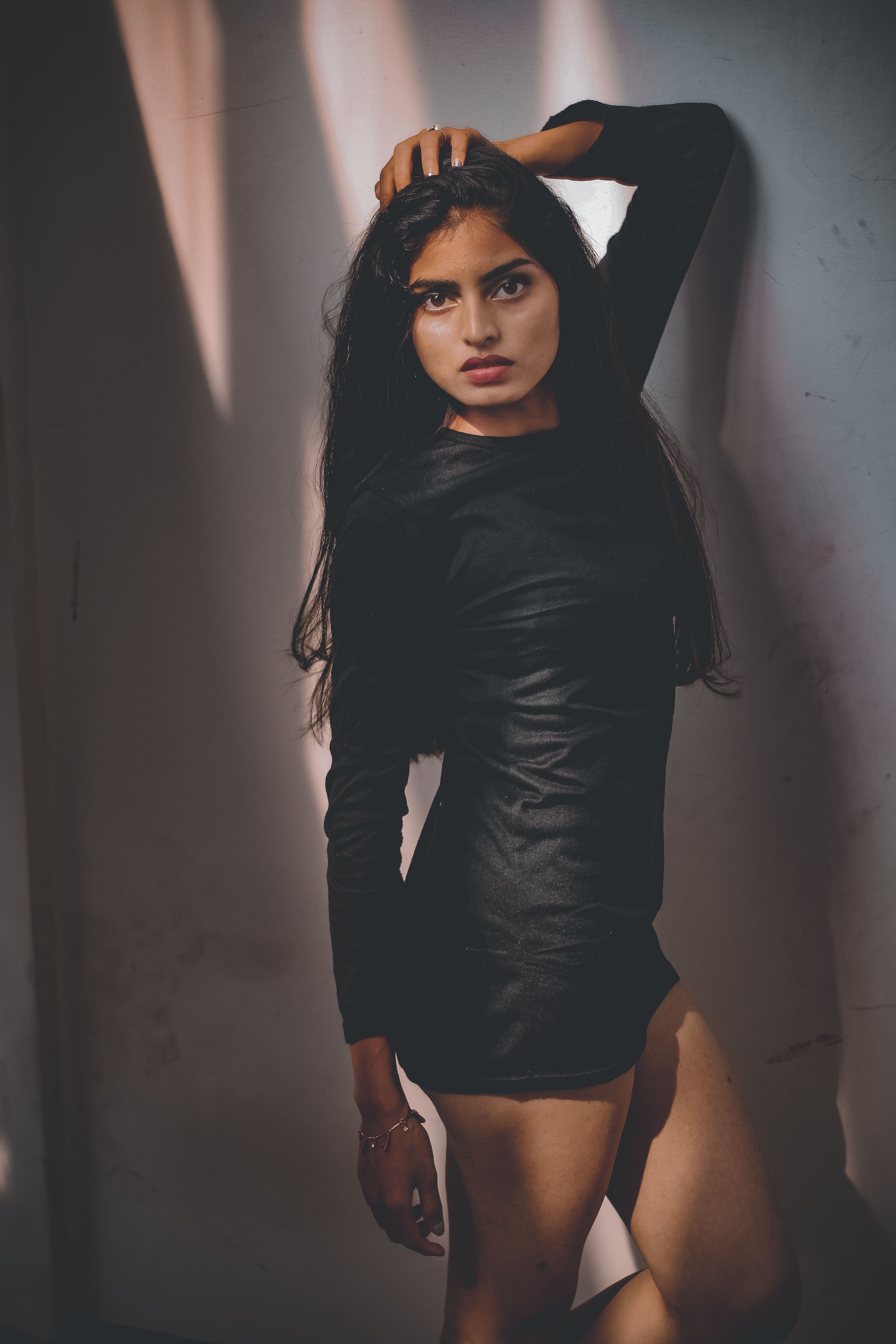 Portrait of a young woman in a black dress posing confidently indoors with dramatic lighting.