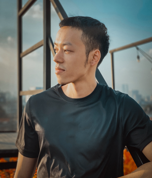 Portrait of a young man wearing a black shirt, set against the Hanoi cityscape. Outdoor scene in daylight.