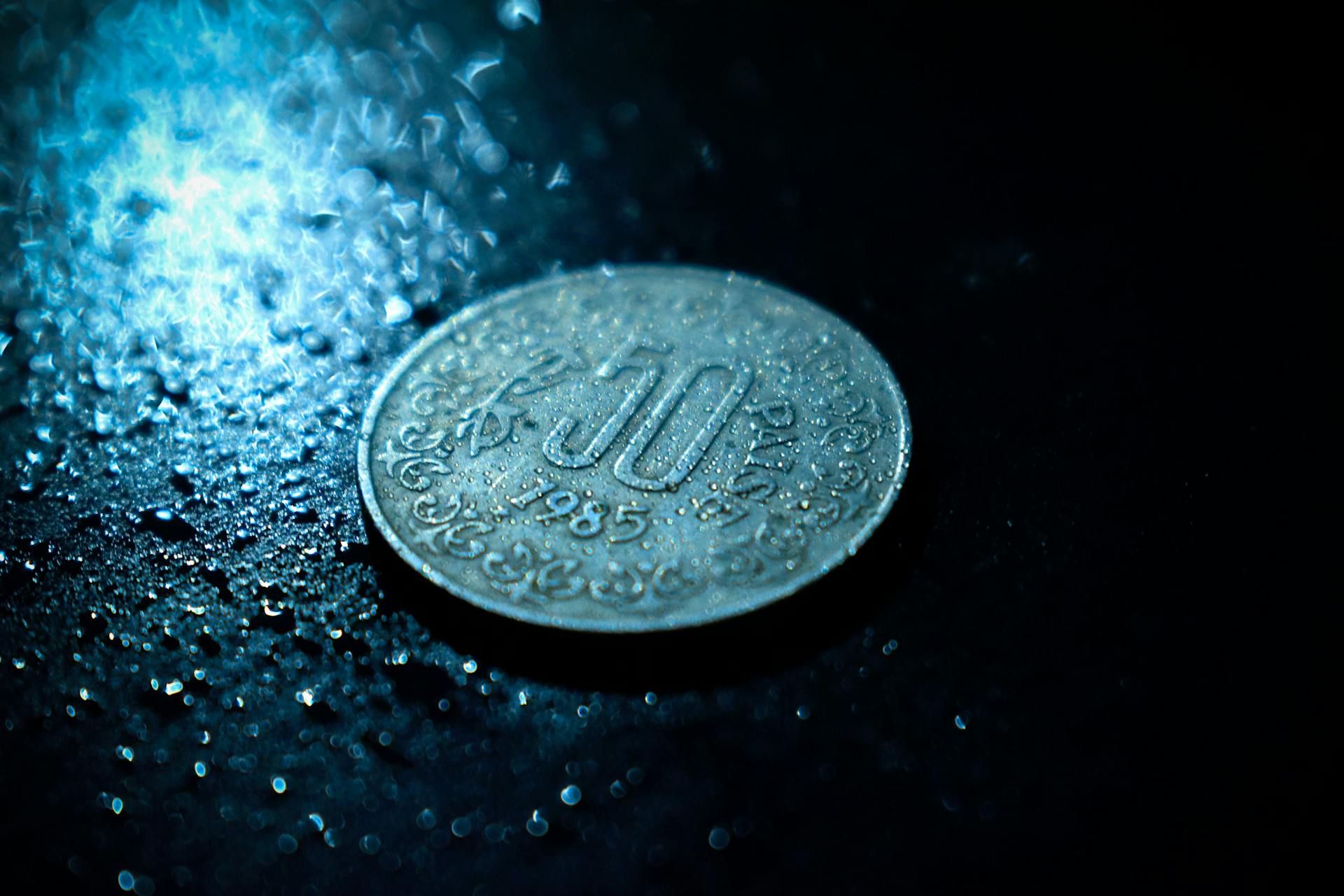 Close-up of a vintage 1985 coin on a wet, textured surface with dramatic lighting.