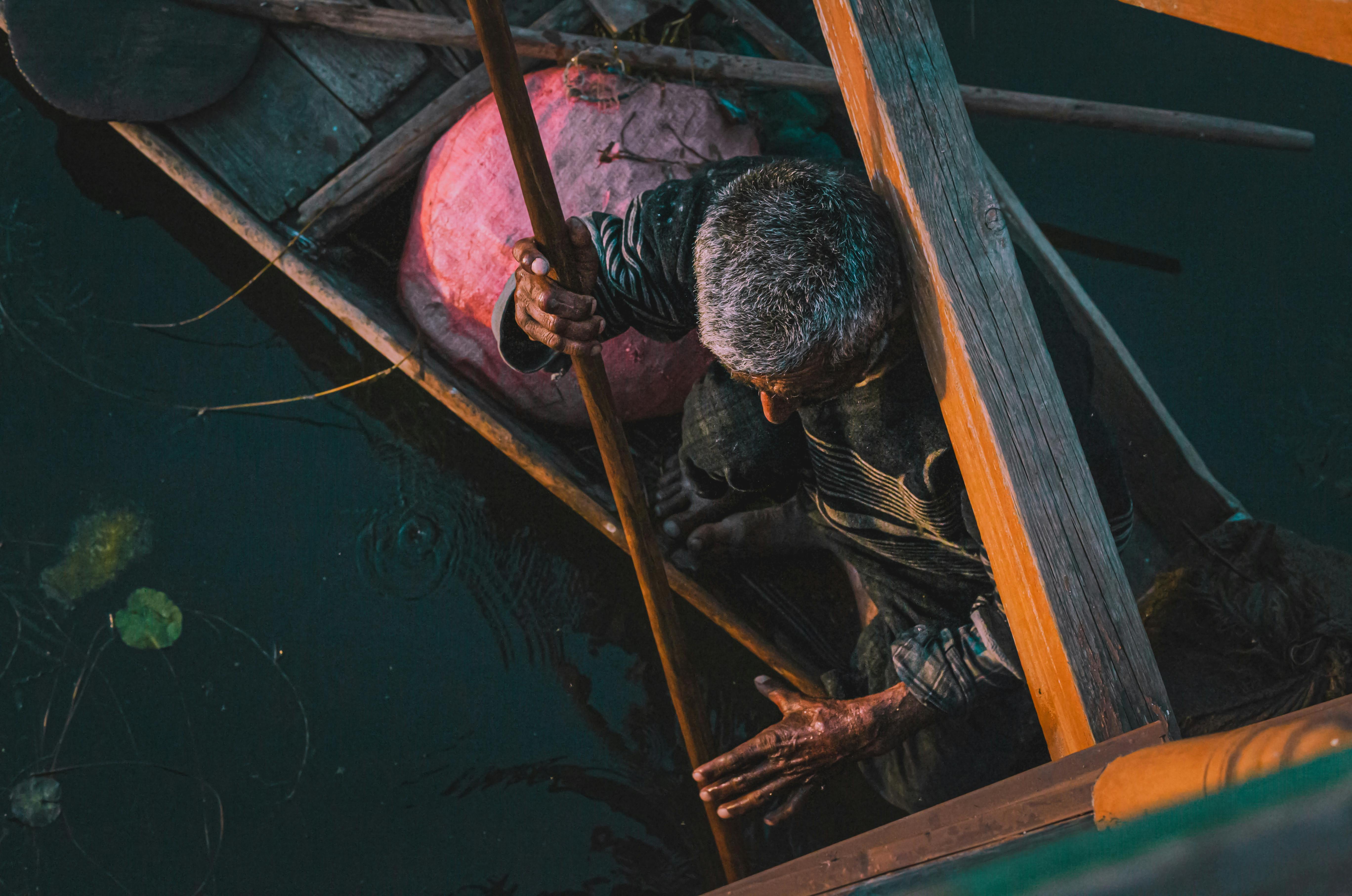 Free A senior man skillfully rowing a wooden boat in tranquil waters viewed from above. Stock Photo