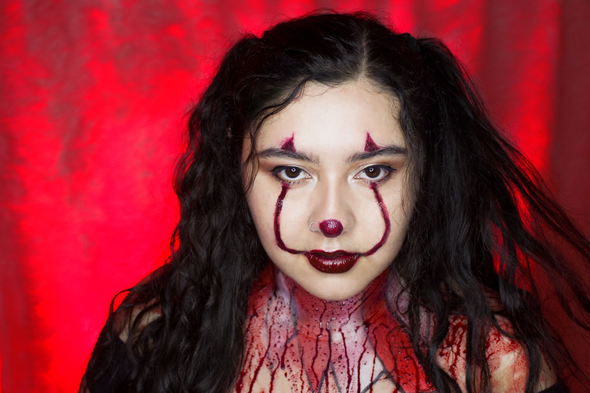 Close-up portrait of a woman with artistic clown makeup featuring a vivid red background, perfect for Halloween themes.