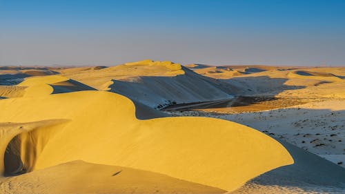 Picturesque landscape of endless desert valley with steep sandy dunes against cloudless sunset sky