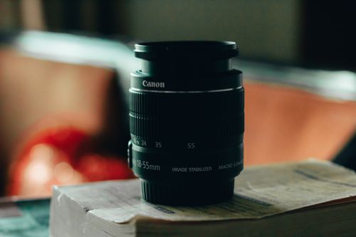 Free A Canon camera lens placed on a book, captured with soft focus, indoors. Stock Photo