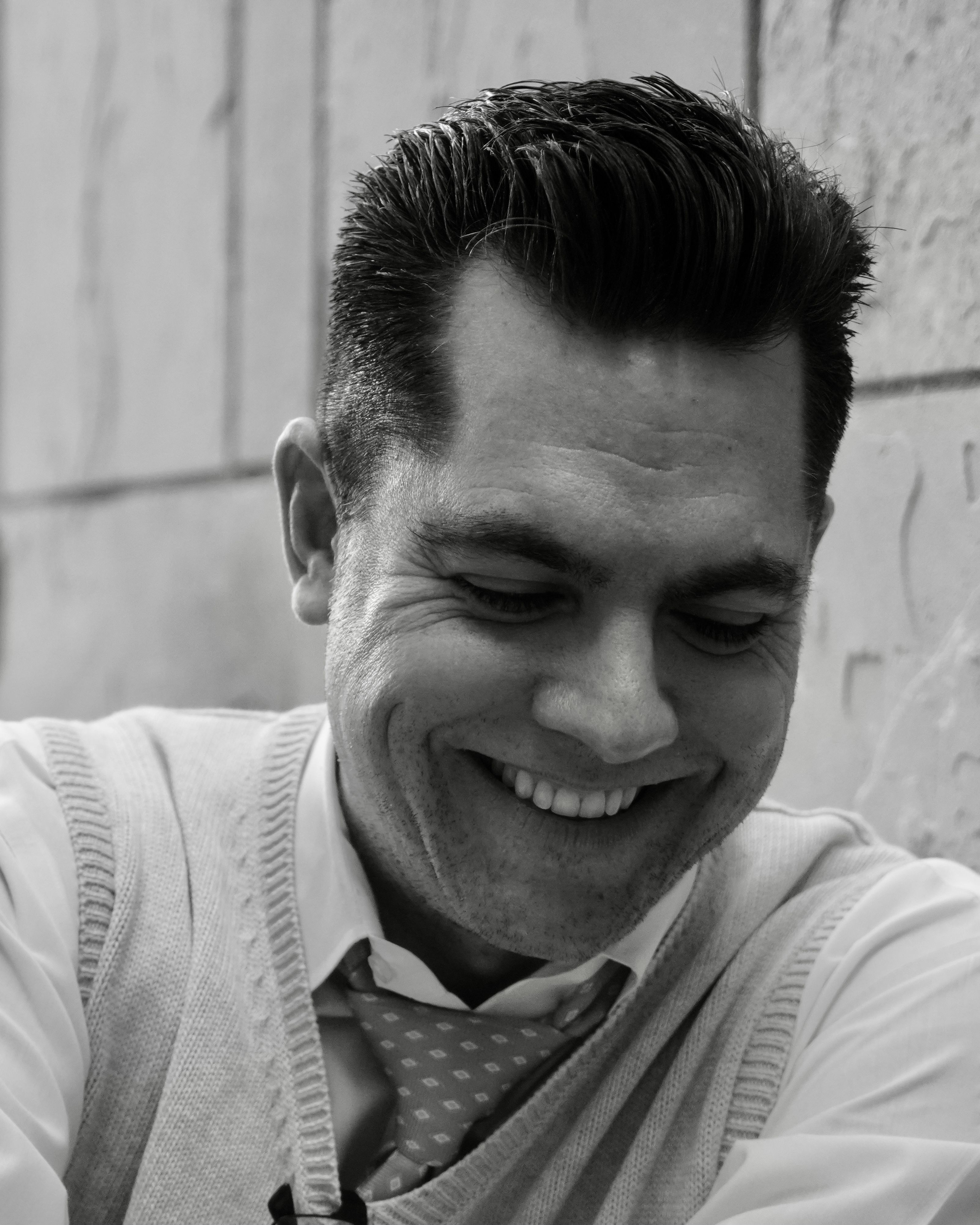 Black and white portrait of a smiling man in a formal outfit against a textured wall.