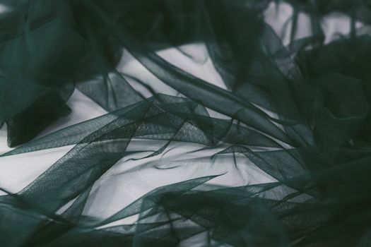 Close-up of a soft, dark green sheer fabric creating elegant abstract patterns.