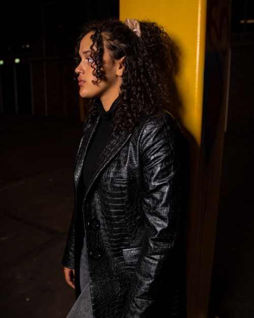 Free Stylish woman with curly hair in a leather jacket leans against a pole at night in Amsterdam. Stock Photo