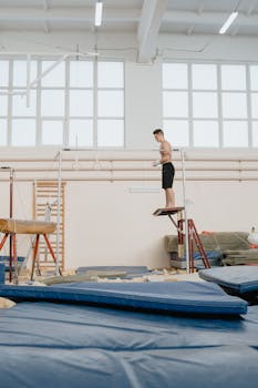 A shirtless male gymnast on a platform preparing for parallel bars routine in a gym.