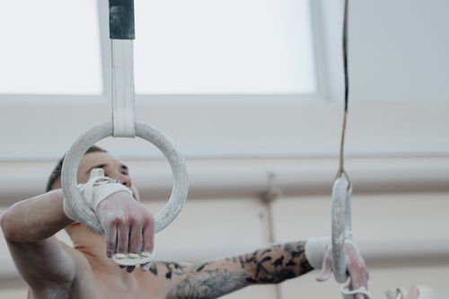 Free Close-up of a gymnast with tattooed arm holding gymnastic rings indoors. Stock Photo