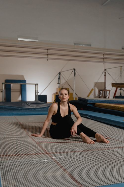 Free Caucasian woman sitting barefoot on a trampoline in a gym, wearing activewear and smiling. Stock Photo