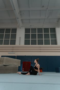 Caucasian woman in a gym sitting barefoot near gym mats, portraying fitness and relaxation.