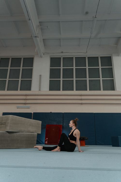 Free Caucasian woman in a gym sitting barefoot near gym mats, portraying fitness and relaxation. Stock Photo