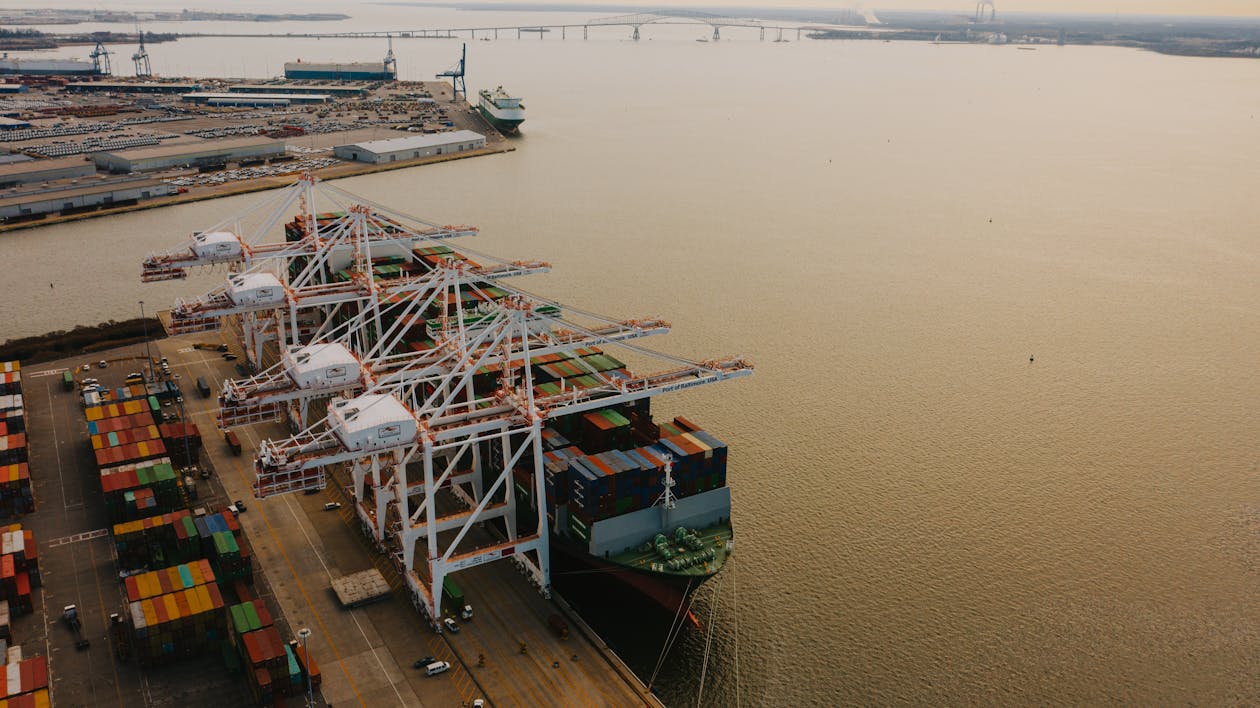 Drone view of cargo containers loaded on long ship on river of pier with lifting cranes