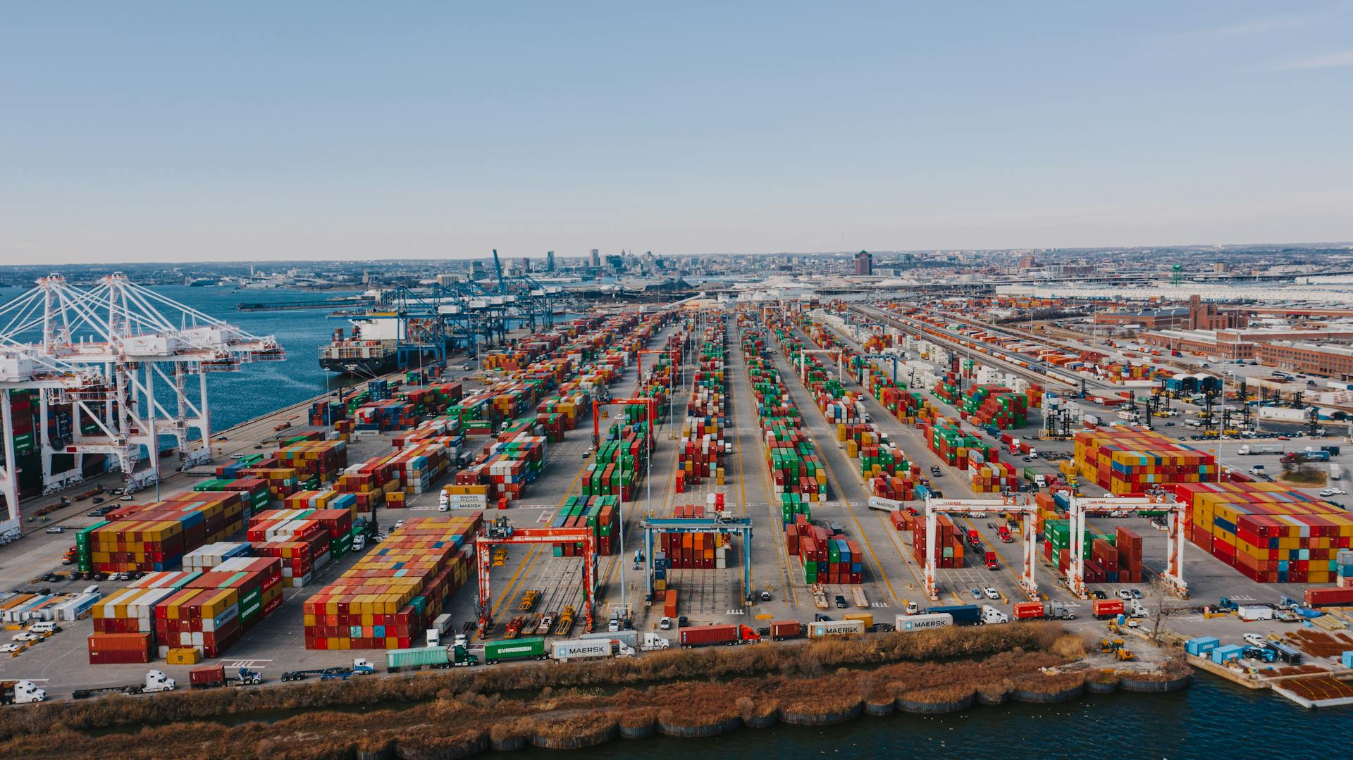 Drone view of river embankment with various bright cargo containers near steel lifting cranes under cloudless sky