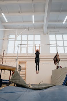 A young gymnast exercises on the uneven parallel bars in an indoor gym setting.
