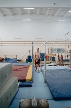 A male gymnast prepares for a routine on indoor parallel bars in a well-equipped gym.