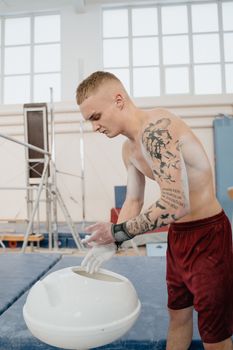 Young shirtless gymnast with arm tattoos preparing for training indoors.