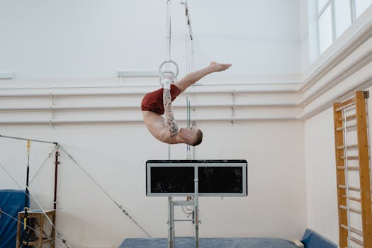 A skilled male gymnast performing an exercise on gymnastics rings in a well-lit indoor gym.