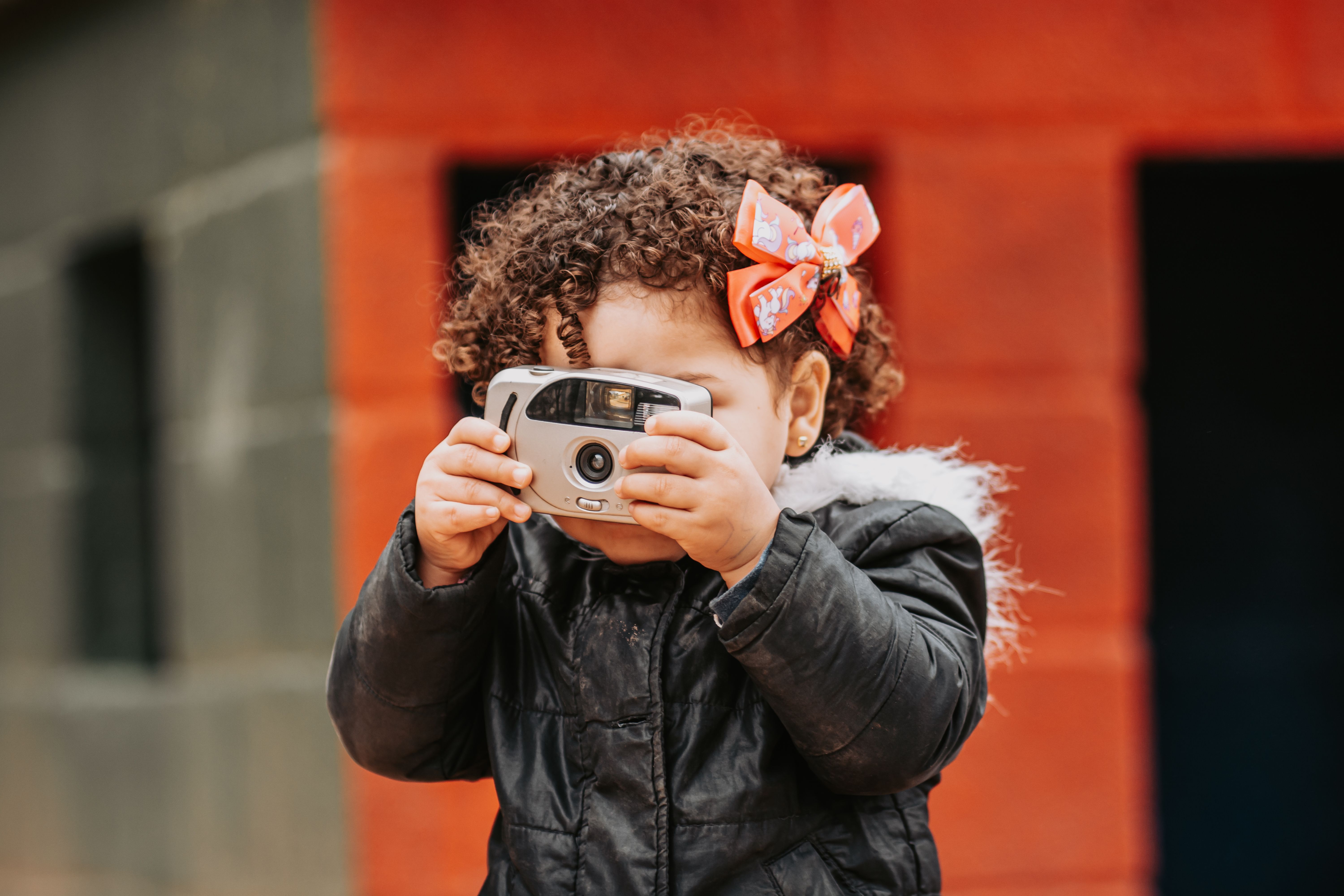 A young child capturing moments with a vintage camera outdoors. Playful and curious.