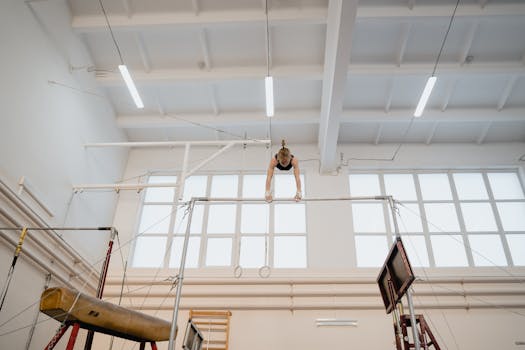 Young female gymnast skillfully practicing on uneven bars in a bright gym setting.