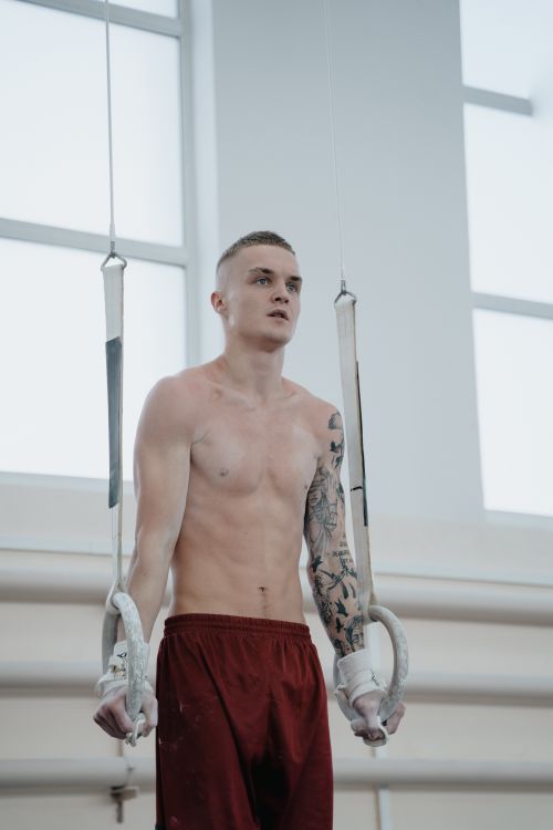 Free Tattooed male gymnast performing routines on rings indoors, showcasing strength and focus. Stock Photo