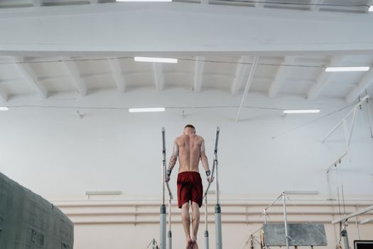 A male gymnast performs on parallel bars indoors, showcasing strength and balance.