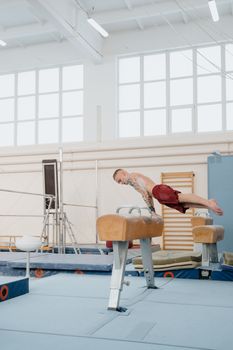 An athletic man practicing gymnastic skills on a pommel horse indoors.