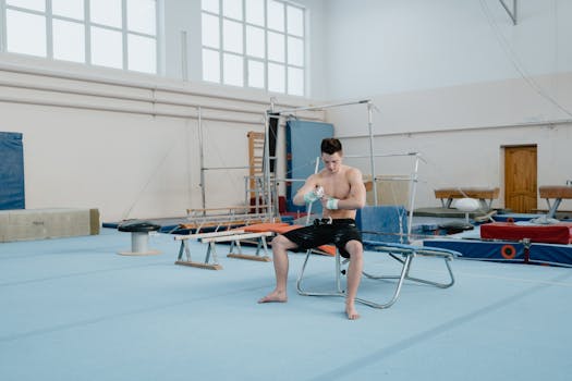Shirtless young male gymnast preparing grips in an indoor training gym.