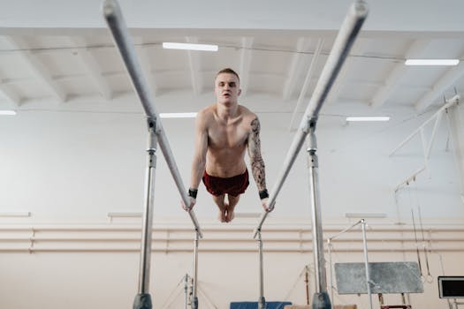 Focused male gymnast shows strength and balance on parallel bars indoors.