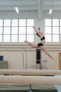 A female gymnast demonstrates a leap in an indoor training facility, showcasing strength and grace.