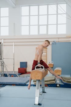 Young male gymnast performing on pommel horse in an indoor gym setting, showcasing skill and balance.