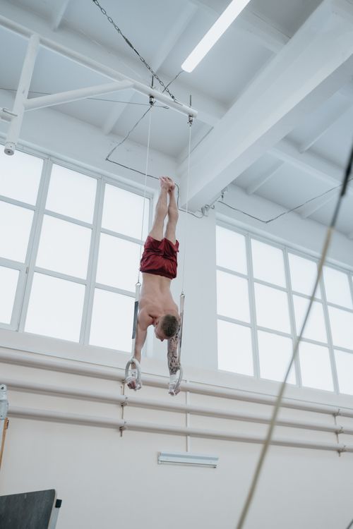 Free Male gymnast demonstrating skill on gymnastic rings upside down indoors. Stock Photo